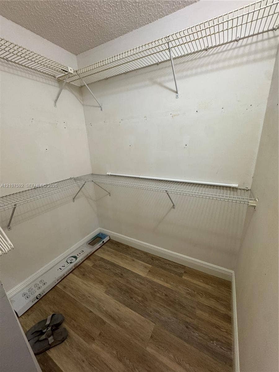Walk-in storage space featuring wood-finish flooring and tiered metal wire shelving