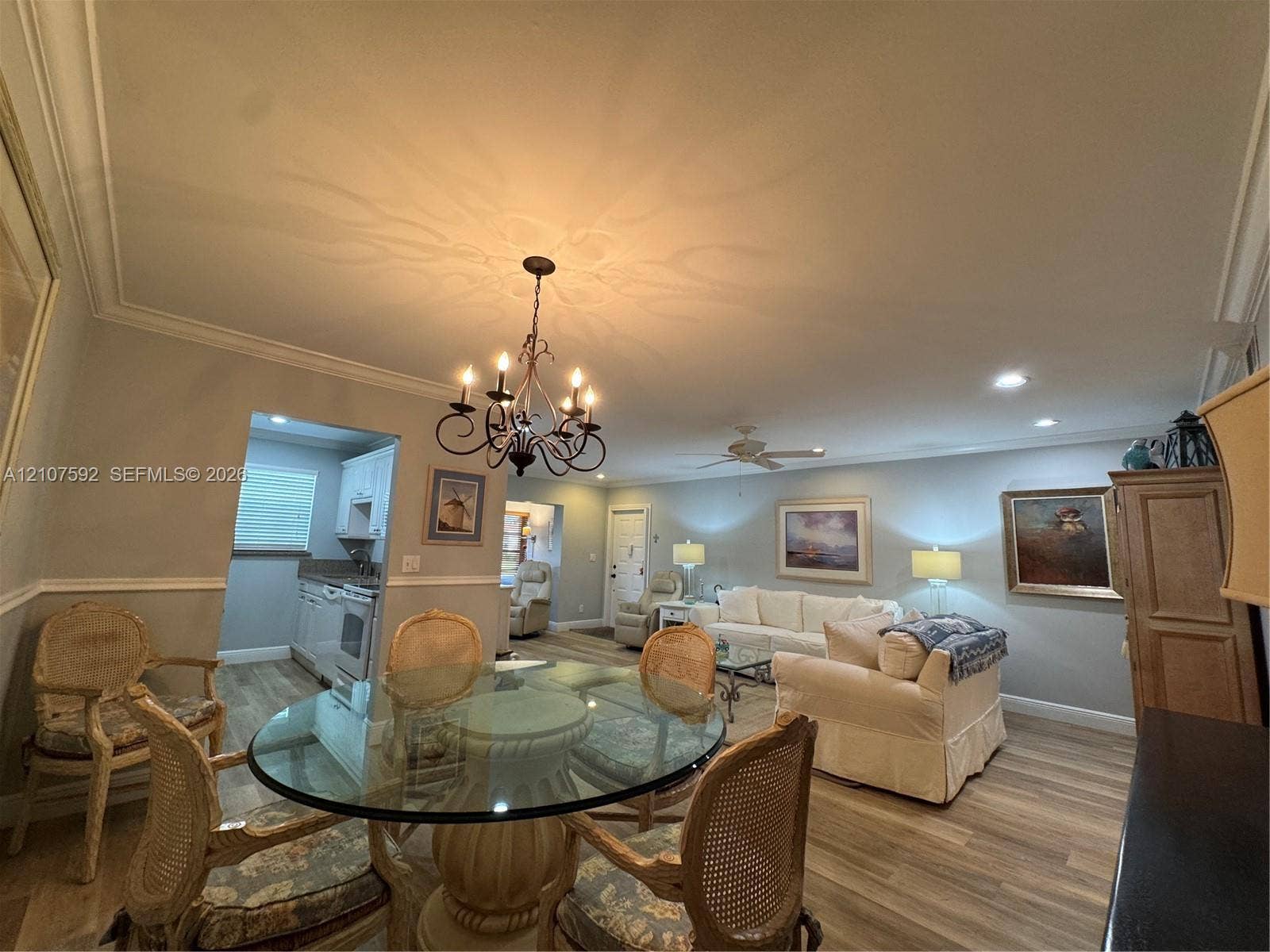 Open-concept room featuring wood-finish flooring, crown molding, chair rail trim, and a decorative wrought-iron chandelier