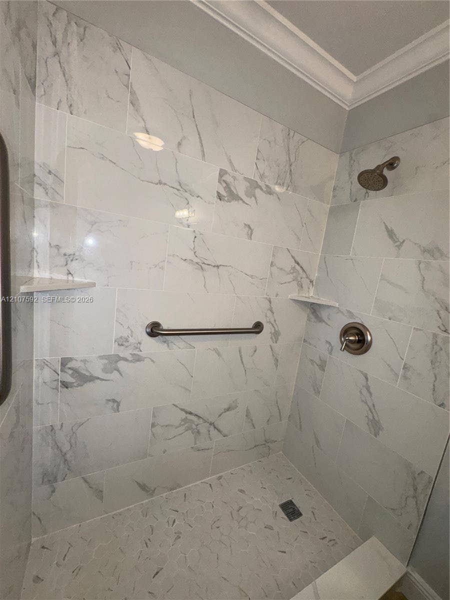 Shower enclosure featuring large-format wall tile with a neutral veined pattern, built-in corner shelving, stone-texture floor tiling, and a metallic finish shower head with matching control handle