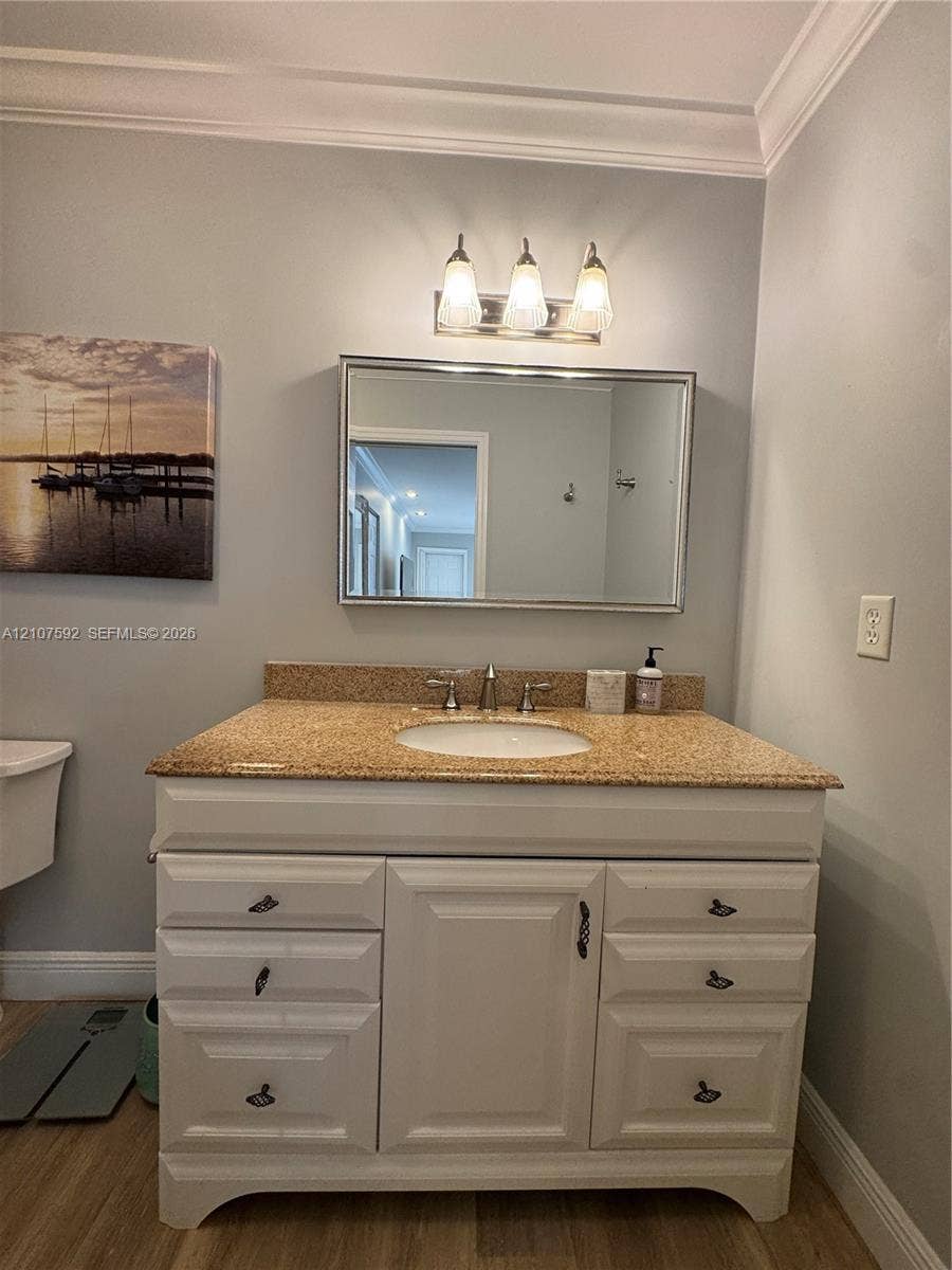 White cabinetry vanity featuring an integrated oval basin, speckled stone-finish countertop, three-light polished chrome fixture, and a framed wall-mounted mirror