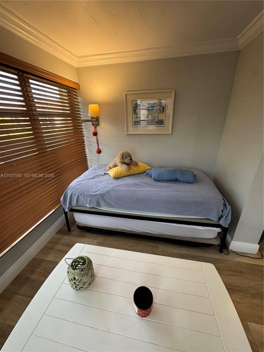 Wood-finish flooring, crown molding, and horizontal wood blinds paired with a wall-mounted light fixture