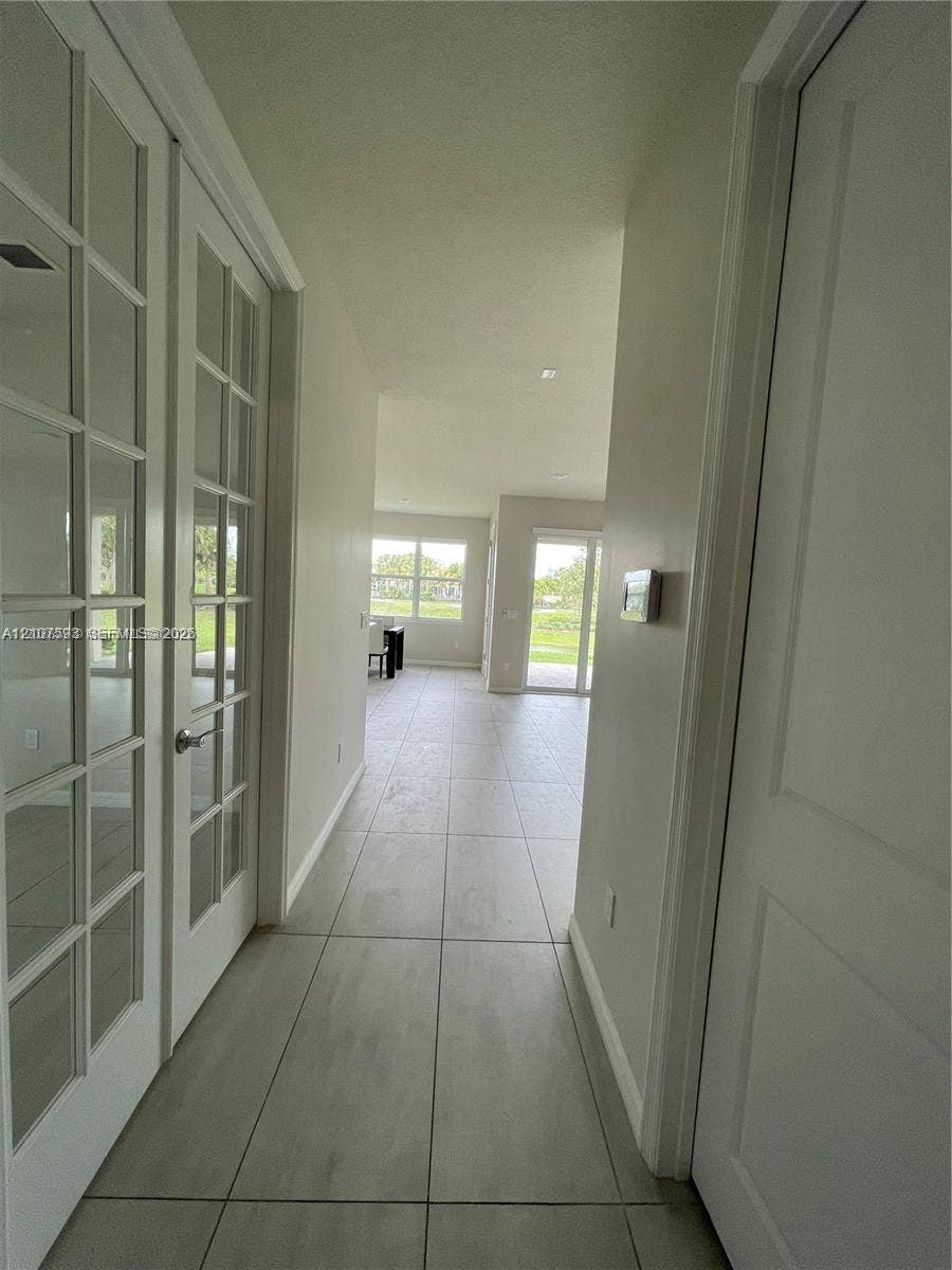 Interior hallway featuring large-format tile flooring, double French doors with glass panes, and multiple windows