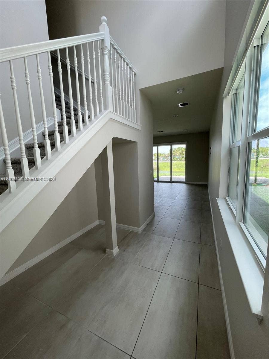 Staircase with white spindle railing, large-format tile flooring, double-height ceiling, and glass sliding doors