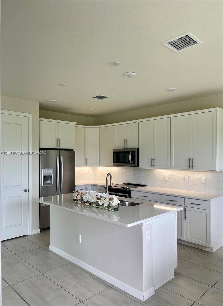 Kitchen featuring white shaker-style cabinetry, quartz countertops, a center island with undermount sink, stainless steel appliances, and under-cabinet lighting