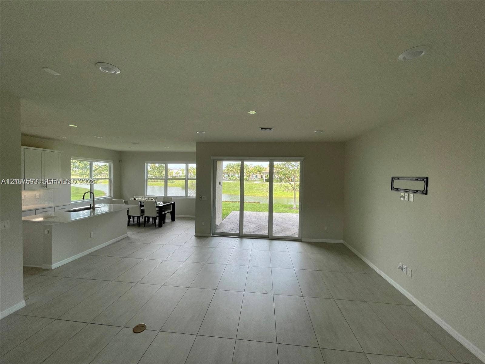 Open-concept interior with large-format tile flooring, recessed lighting, white cabinetry, solid-surface kitchen island, and glass sliding doors providing access to a paved patio