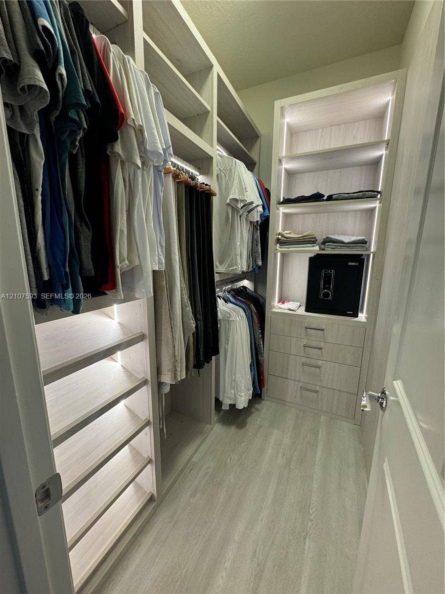 Custom walk-in closet featuring light-toned wood-finish cabinetry, floor-to-ceiling shelving, integrated vertical lighting, and a built-in four-drawer dresser