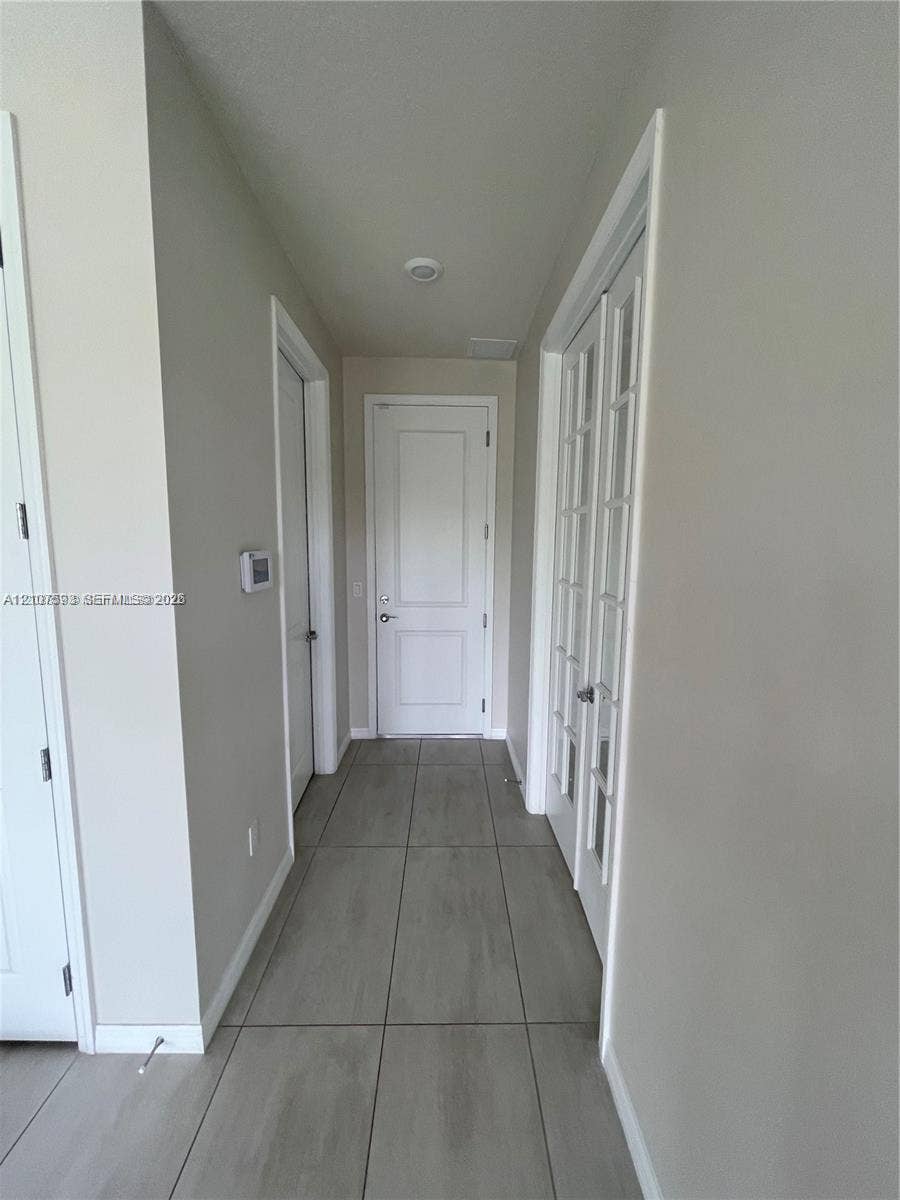 Neutral-toned interior hallway featuring large-format ceramic floor tiles, multi-panel solid doors, and a set of French doors with glass panes