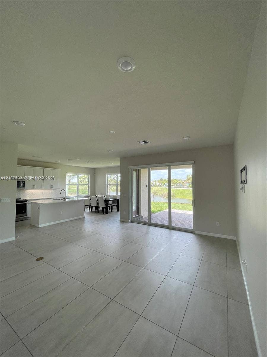 Large-format tile flooring, recessed lighting, kitchen with white cabinetry and an island, and sliding glass doors opening to a paved patio