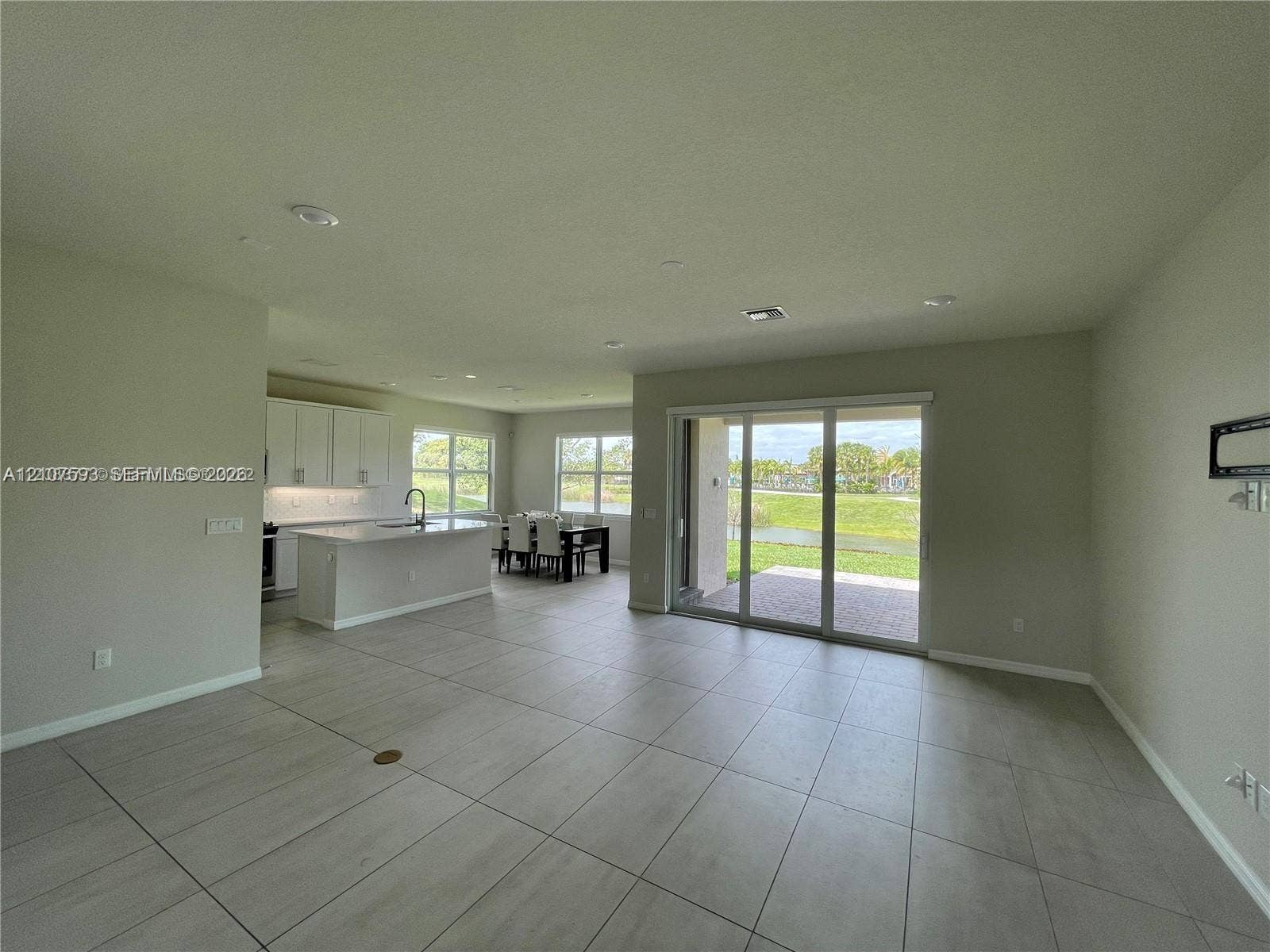 Open-concept interior featuring large-format tile flooring, recessed lighting, kitchen with white cabinetry and quartz-surfaced island, and sliding glass doors with exterior access
