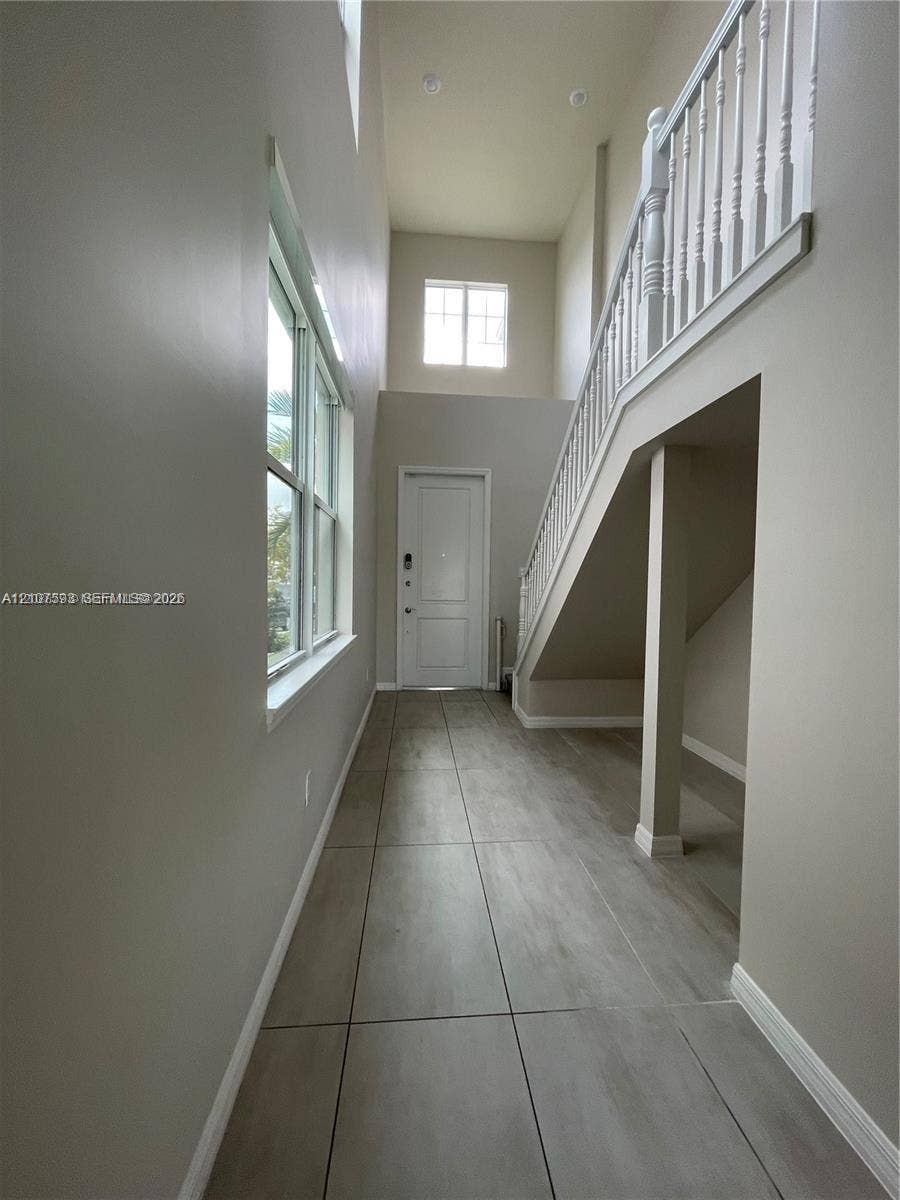 High-ceiling entryway featuring neutral wall tones, large-format tile flooring, multi-pane windows, and a staircase with a white wood-finish balustrade