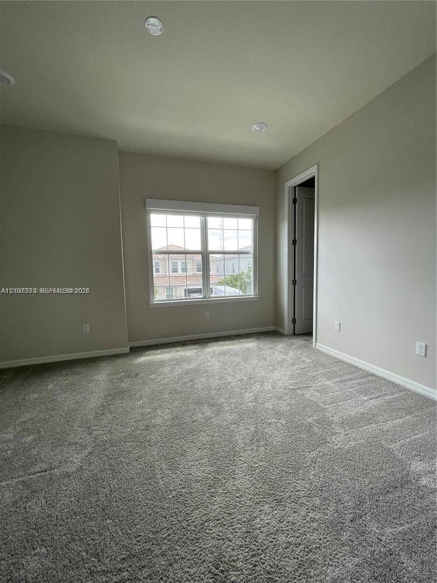 Neutral-toned interior space featuring wall-to-wall carpeting, recessed ceiling lighting, and a multi-pane window with white trim
