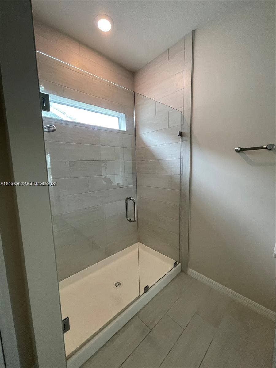 Walk-in shower featuring a frameless glass enclosure, horizontal tiled wall finish, recessed lighting, and a transom window