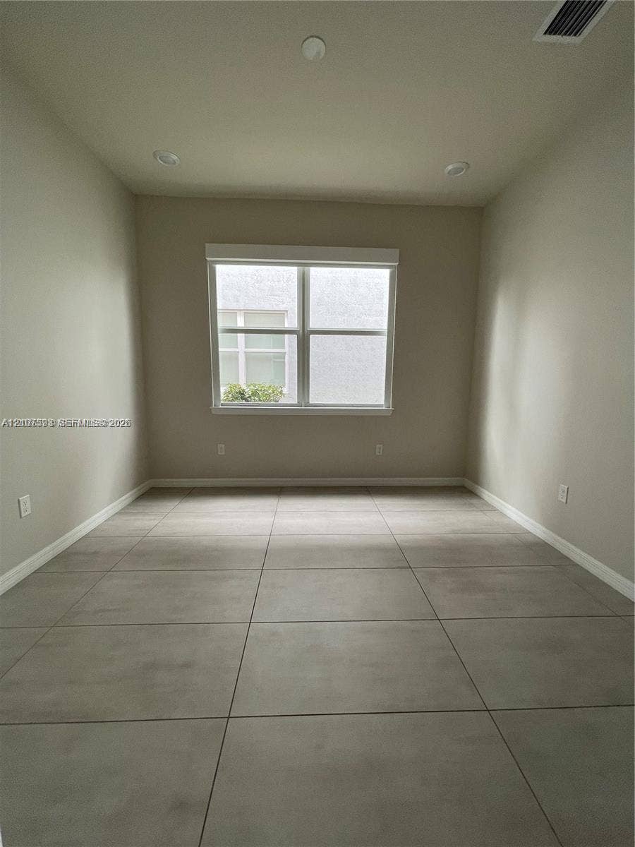 Neutral-toned interior room featuring large-format ceramic tile flooring, recessed ceiling lighting, and a dual-pane window with a frame-integrated blind
