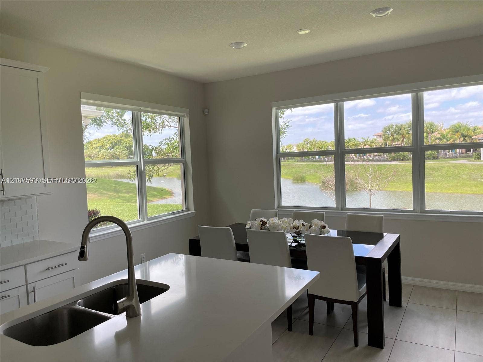 Kitchen featuring a central island with a double-basin sink, high-arc faucet, quartz countertops, white cabinetry, and tile flooring