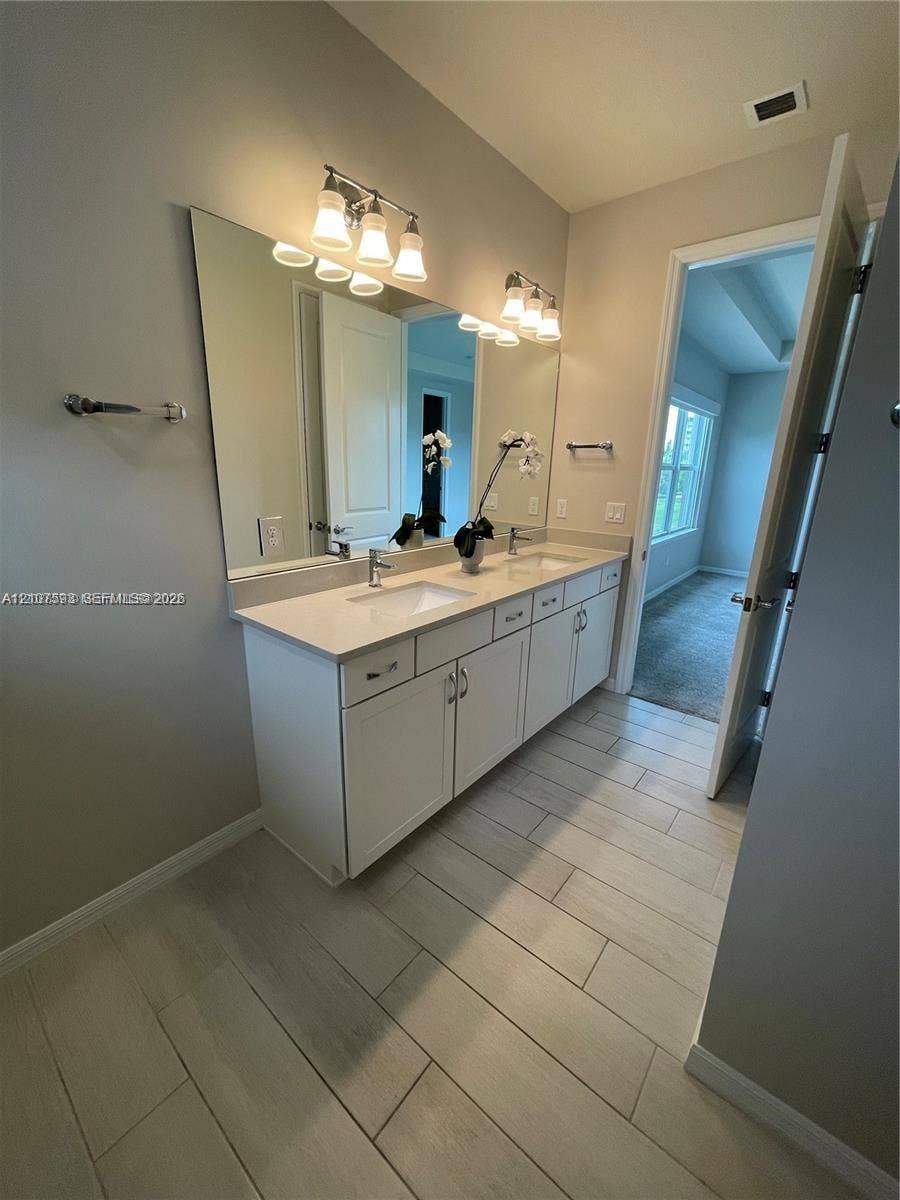 Double vanity featuring a light-toned countertop, rectangular undermount sinks, chrome fixtures, and a wall-to-wall mirror with dual light fixtures, complemented by light-toned tile flooring