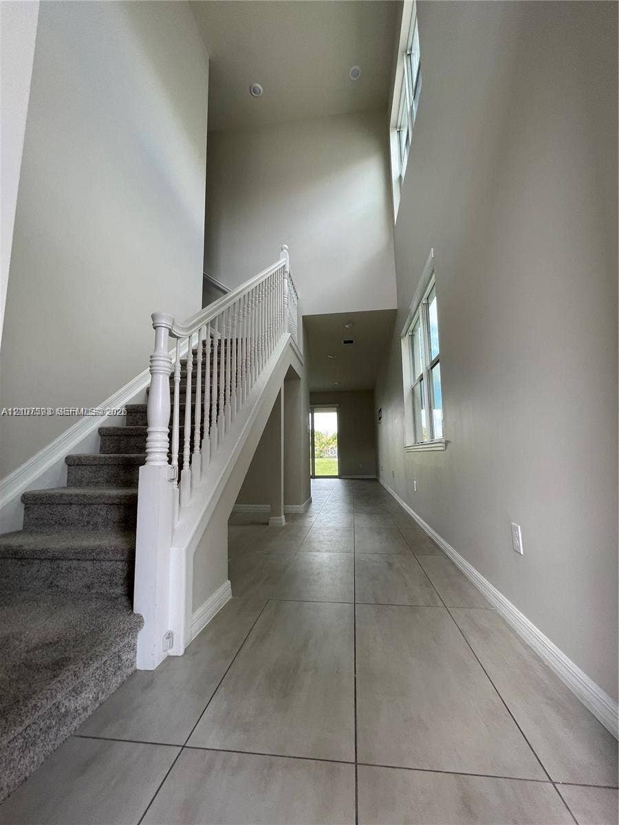 Two-story foyer with high ceilings, large windows, carpeted staircase with white balustrade, and tile flooring