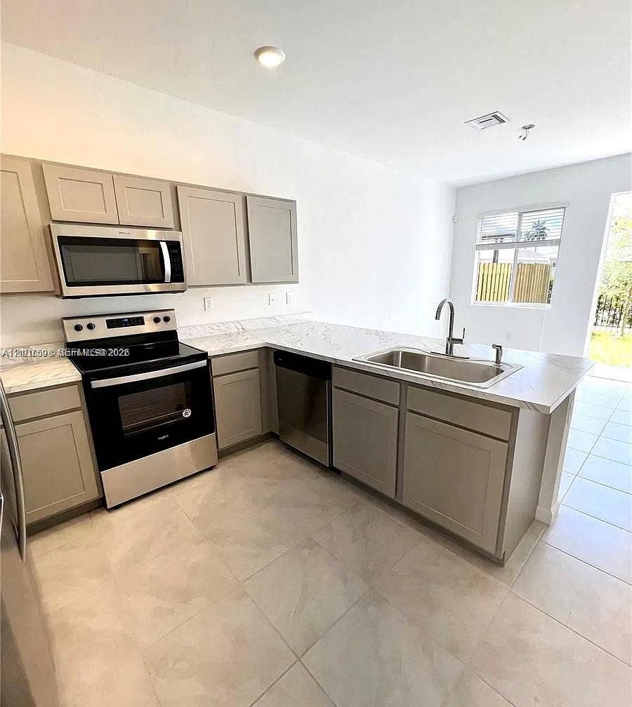 1088 NW 208th Terrace, Miami Gardens, FL 33169 Kitchen featuring neutral-toned shaker cabinetry, stone-patterned countertops, stainless steel appliances, a dual-basin undermount sink with a gooseneck faucet, and large-format tile flooring