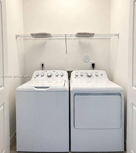 1088 NW 208th Terrace, Miami Gardens, FL 33169 Dedicated laundry alcove featuring side-by-side white top-load washer and dryer with a wire-grid upper shelving unit