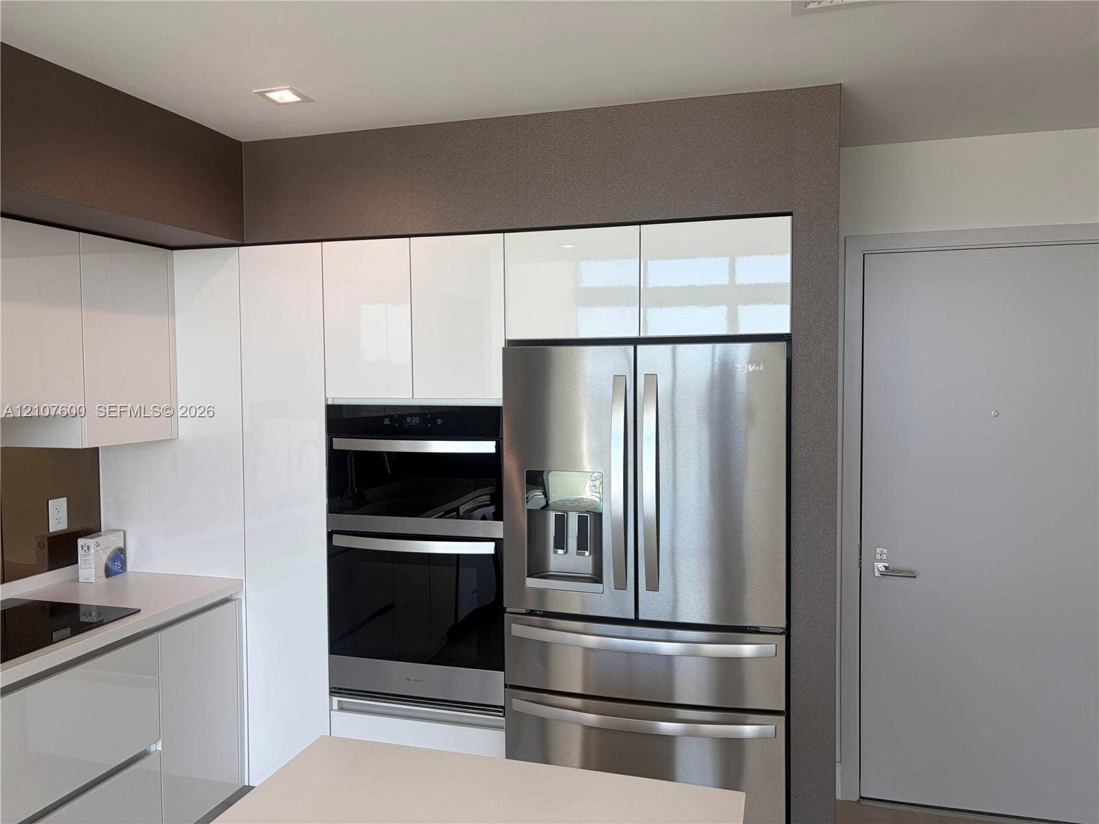Glossy white cabinetry, built-in stainless steel double wall ovens, integrated stainless steel refrigerator, and recessed lighting