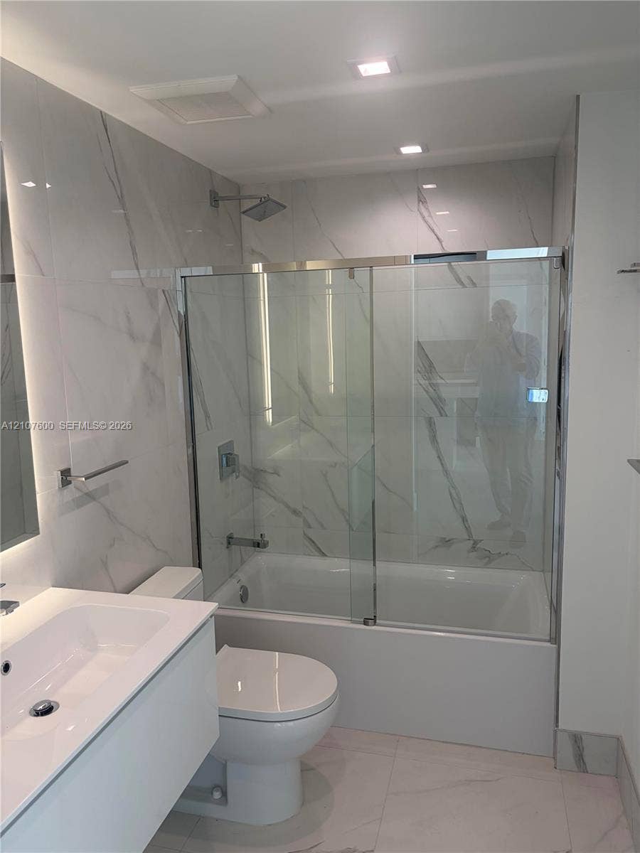 Modern bathroom featuring full-height large-format stone-patterned wall tile, a floating vanity with an integrated basin, and a glass-enclosed shower and tub combination with a square showerhead