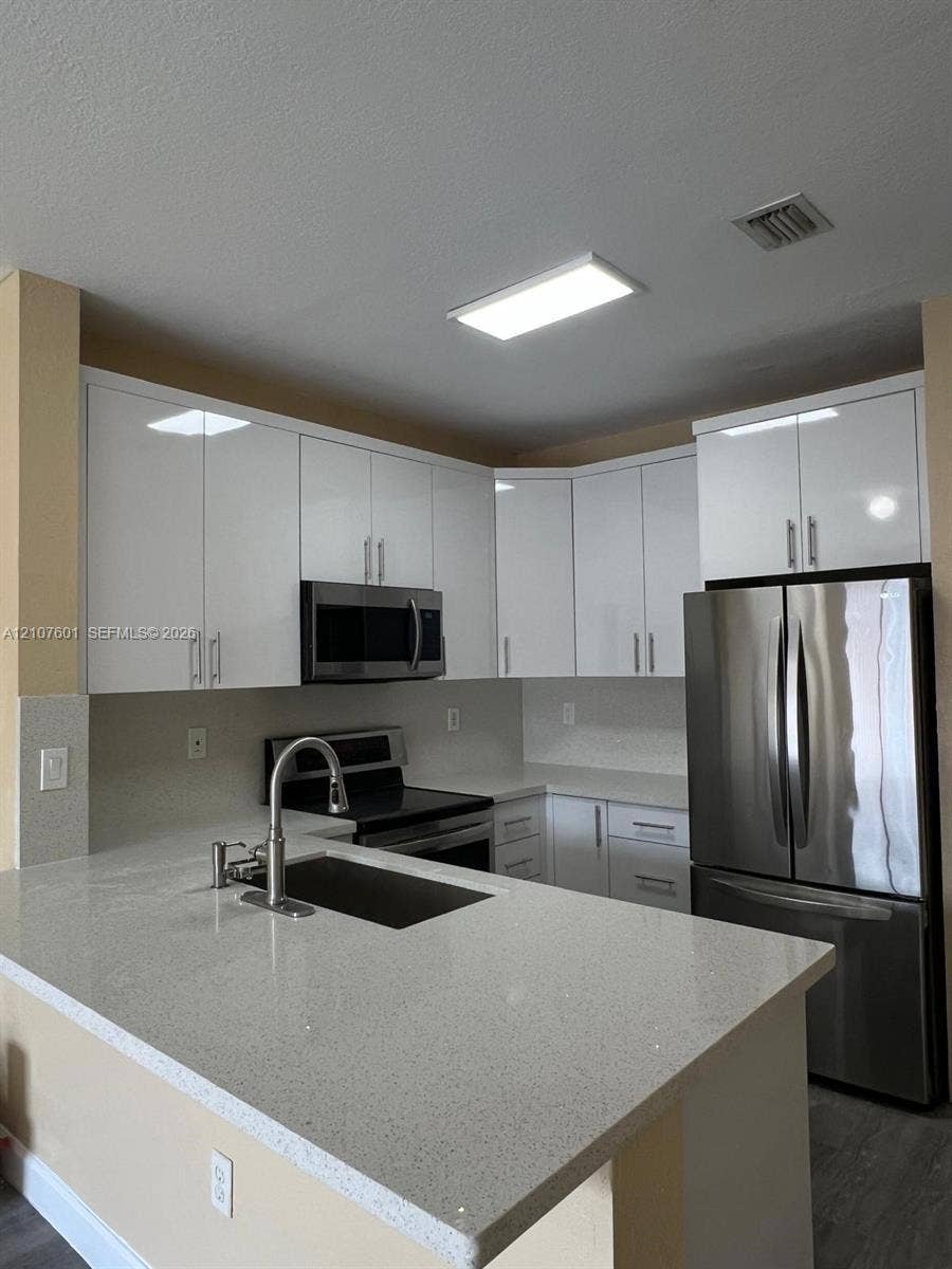 7080 NW 177th Street, #203-13, Hialeah, FL 33015 Kitchen featuring white flat-panel cabinetry, quartz countertops, a stainless steel undermount sink with a gooseneck faucet, and stainless steel appliances