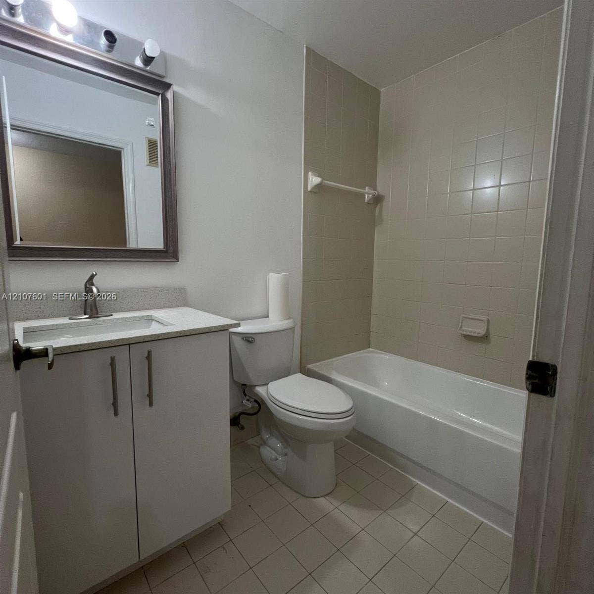 7080 NW 177th Street, #203-13, Hialeah, FL 33015 Bathroom featuring a white vanity cabinet with a stone-composite countertop, undermount sink, ceramic-tile tub surround, and three-bulb vanity lighting