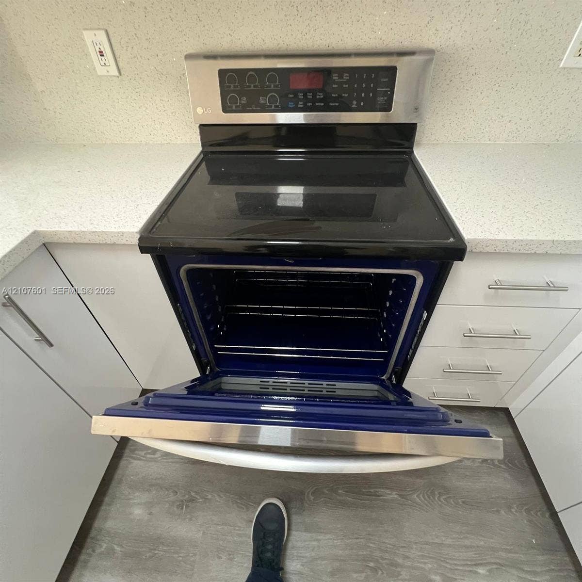 7080 NW 177th Street, #203-13, Hialeah, FL 33015 Stainless steel slide-in electric range featuring a black glass cooktop, solid-surface countertops, white flat-panel cabinetry with brushed nickel hardware, and wood-finish flooring