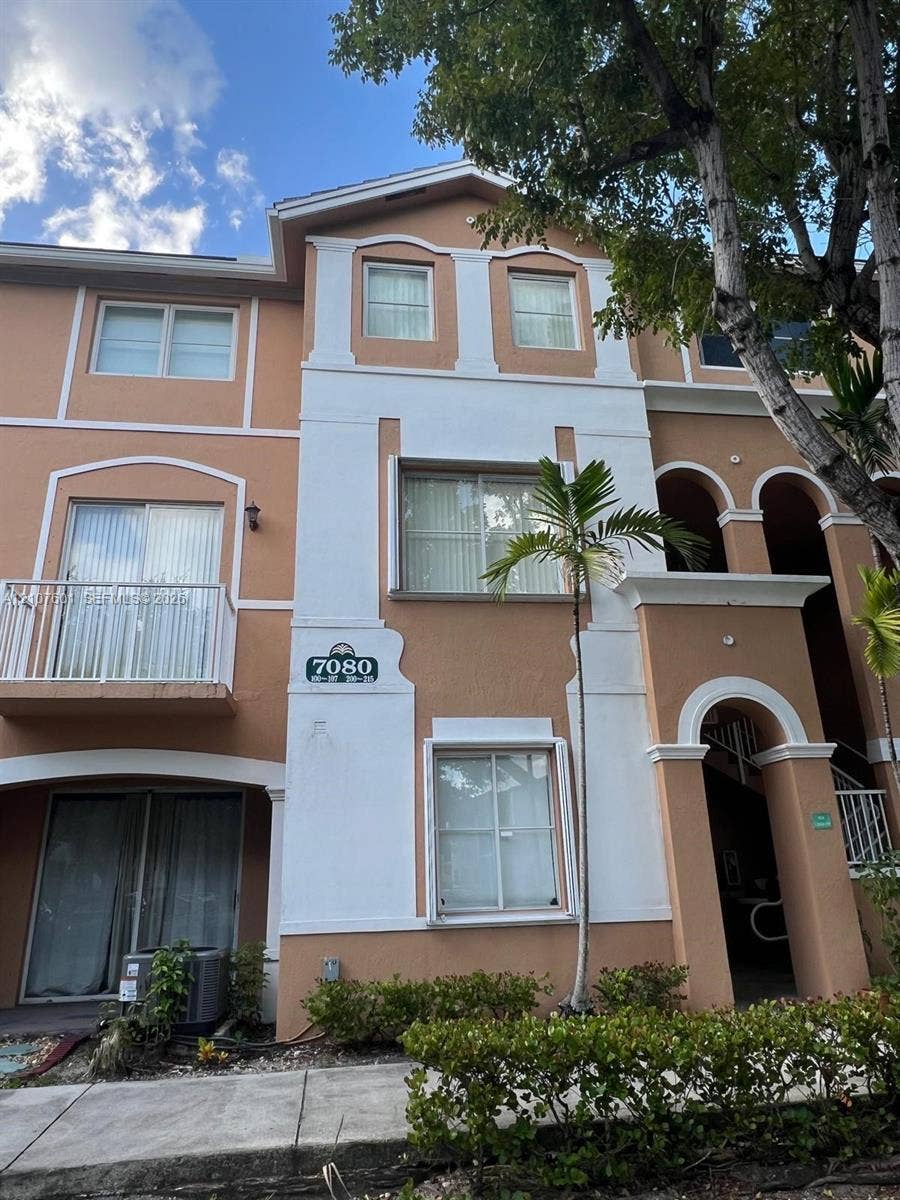 7080 NW 177th Street, #203-13, Hialeah, FL 33015 Multi-story building exterior featuring stucco cladding, arched architectural accents, a private balcony with metal railings, and a covered ground-level entry