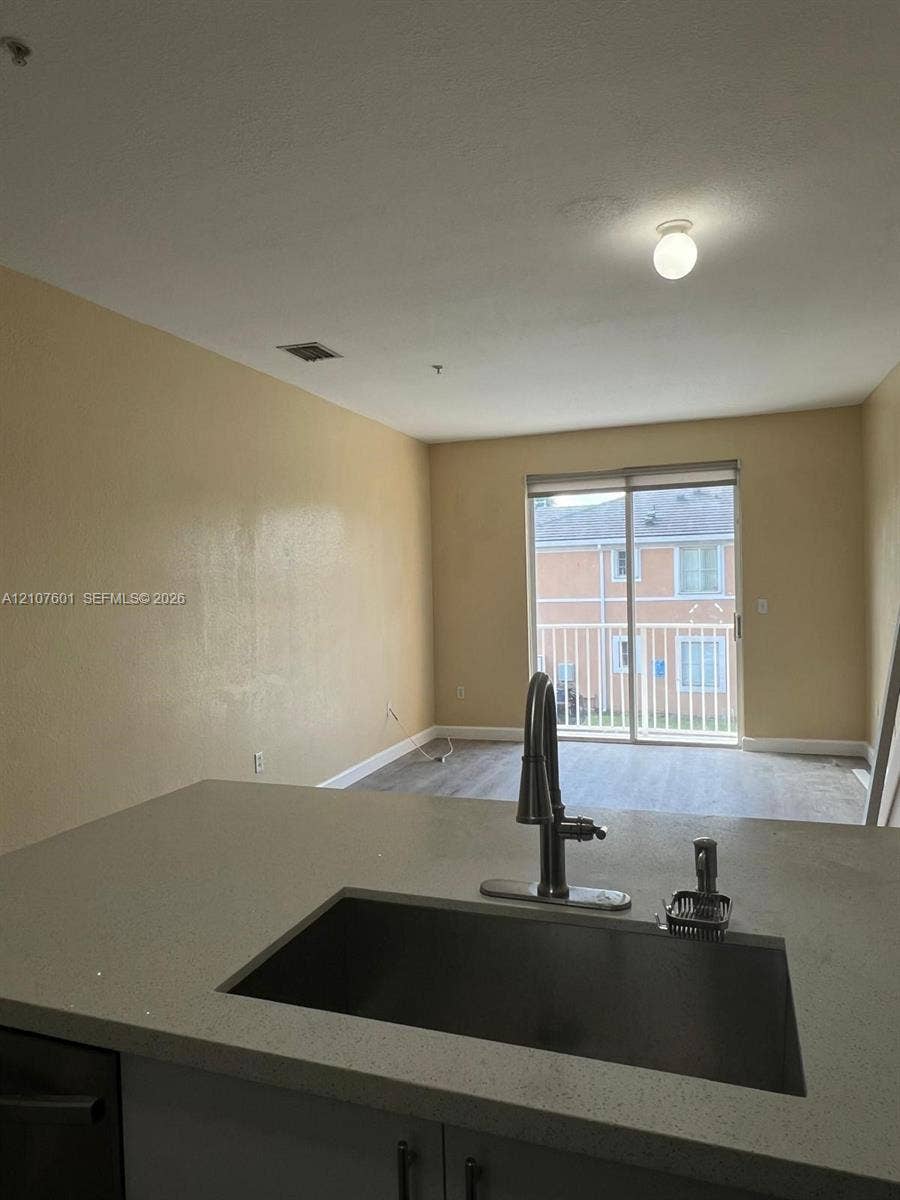 7080 NW 177th Street, #203-13, Hialeah, FL 33015 Kitchen featuring a solid-surface countertop, under-mount stainless steel sink, and high-arc faucet, with wood-finish flooring and a sliding glass door