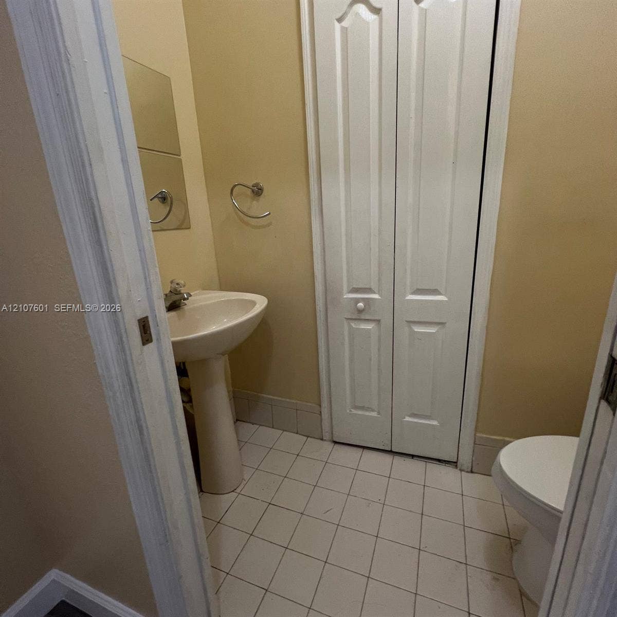 7080 NW 177th Street, #203-13, Hialeah, FL 33015 Pedestal sink with polished metal faucet, tiled flooring, wall-mounted towel ring, and bi-fold door closet