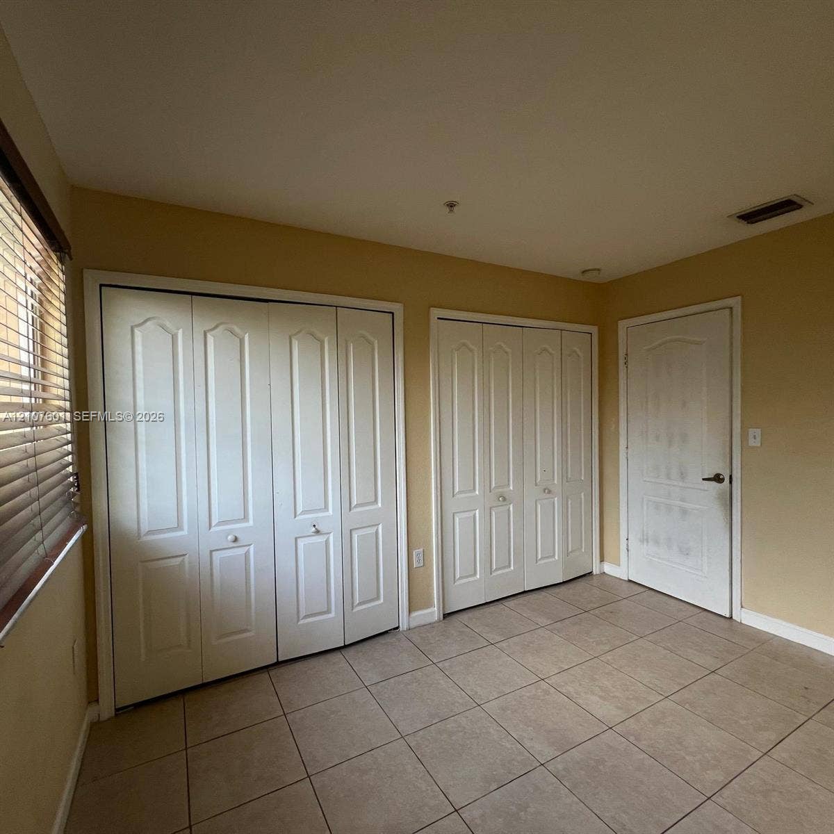 7080 NW 177th Street, #203-13, Hialeah, FL 33015 Room interior featuring tile flooring, dual white bi-fold closet doors, and a single solid-panel interior door