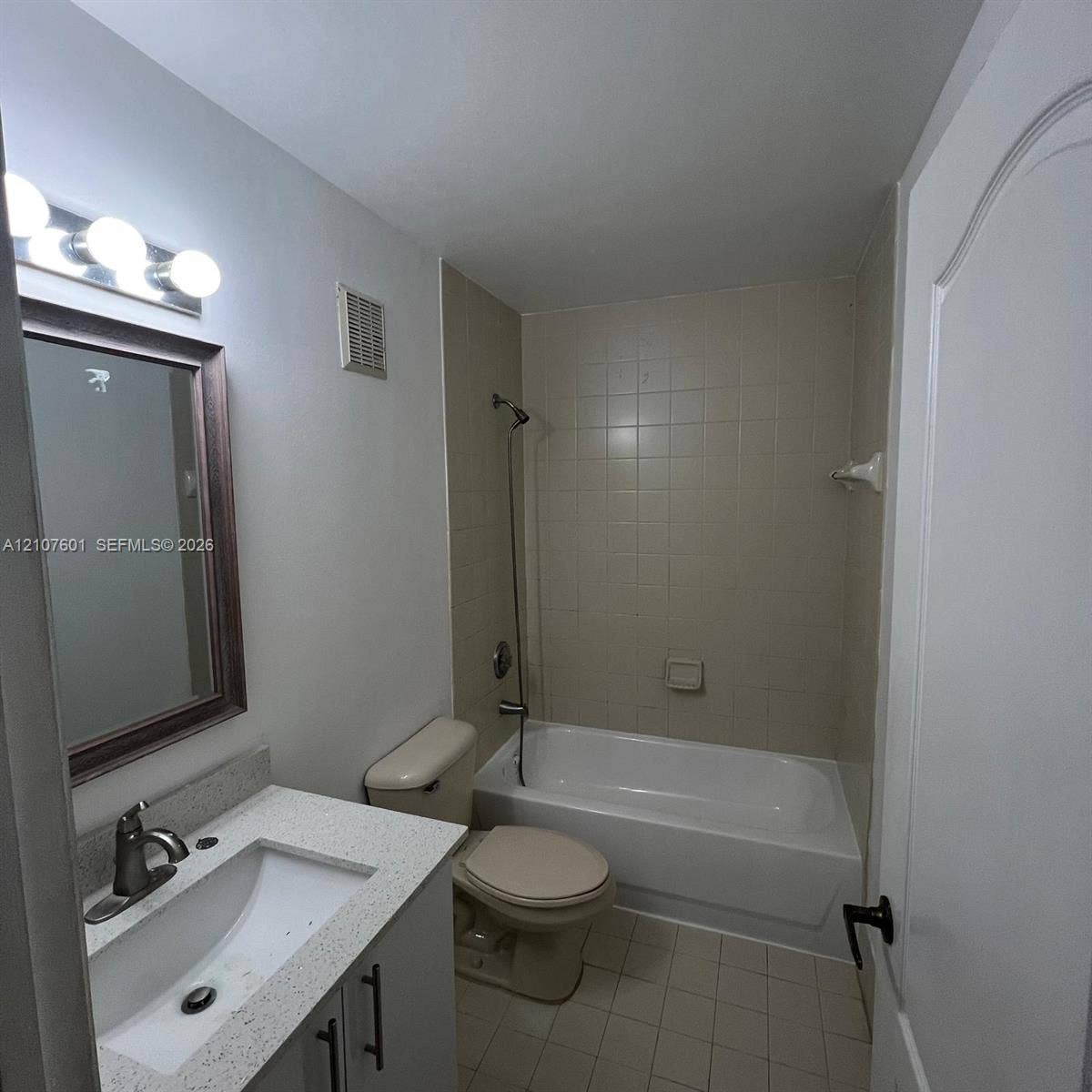 7080 NW 177th Street, #203-13, Hialeah, FL 33015 Bathroom featuring a stone-composite countertop with an integrated basin, three-light vanity fixture, framed wall mirror, and a tub-shower combination with ceramic tile surround