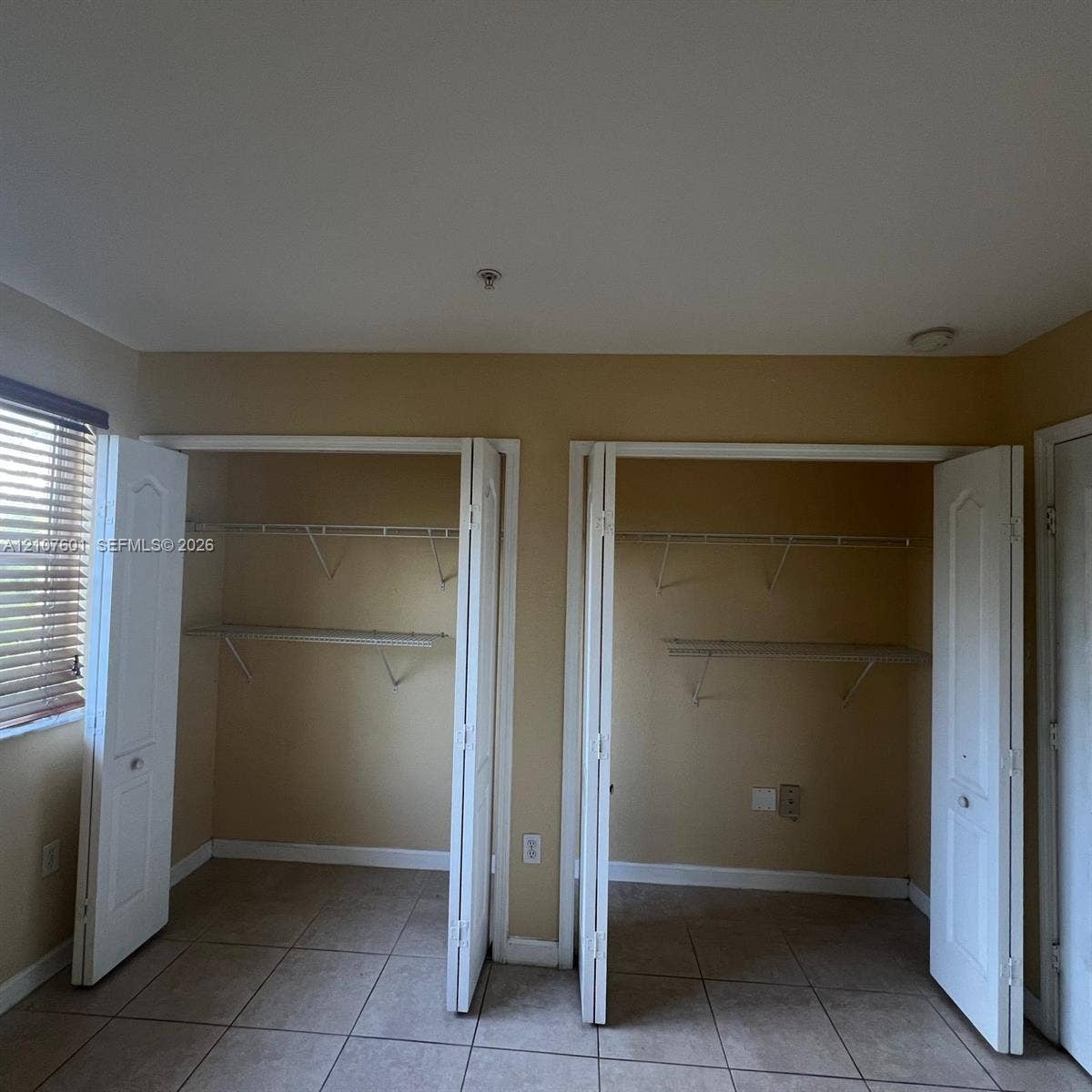 7080 NW 177th Street, #203-13, Hialeah, FL 33015 Dual closets featuring white paneled bifold doors, tile flooring, and integrated wire shelving units