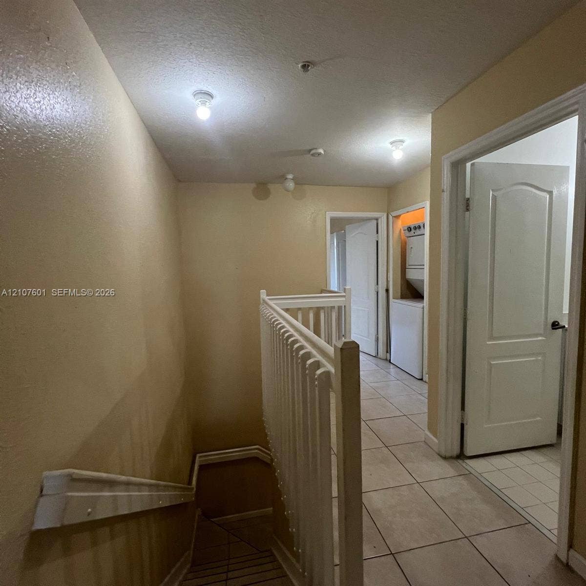 7080 NW 177th Street, #203-13, Hialeah, FL 33015 Staircase featuring a white baluster railing and handrail, neutral ceramic tile flooring, and integrated laundry closet with stacked appliance hookups