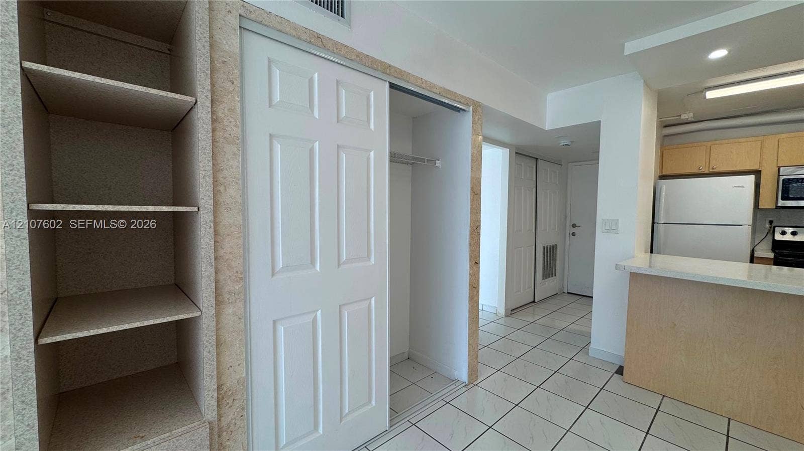 210 172nd Street, #542, Sunny Isles Beach, FL 33160 Built-in shelving, white sliding-door closet, tiled flooring, and breakfast bar with stone-surfaced countertop