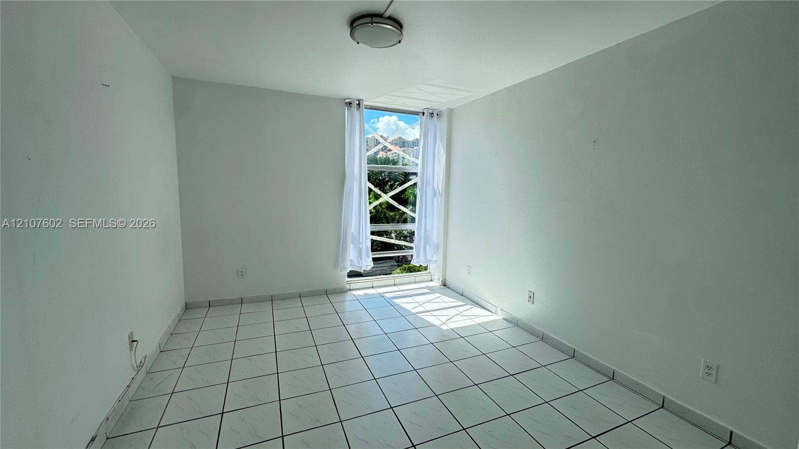 210 172nd Street, #542, Sunny Isles Beach, FL 33160 Neutral interior room featuring white tile flooring, flush-mount lighting, and a floor-to-ceiling window with a cross-pattern security grille