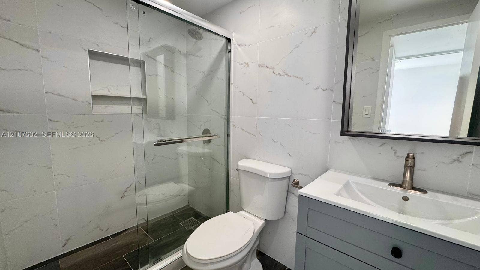 210 172nd Street, #542, Sunny Isles Beach, FL 33160 Full bathroom featuring wall-to-wall large-format porcelain tile, glass-enclosed shower with a recessed wall niche, gray shaker-style vanity with an integrated sink, and a framed mirror