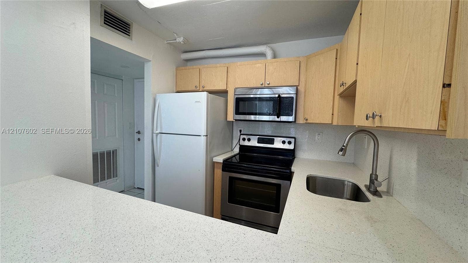 210 172nd Street, #542, Sunny Isles Beach, FL 33160 Kitchen featuring light-finish cabinetry, solid surface countertops, stainless steel appliances, and a stainless steel gooseneck faucet