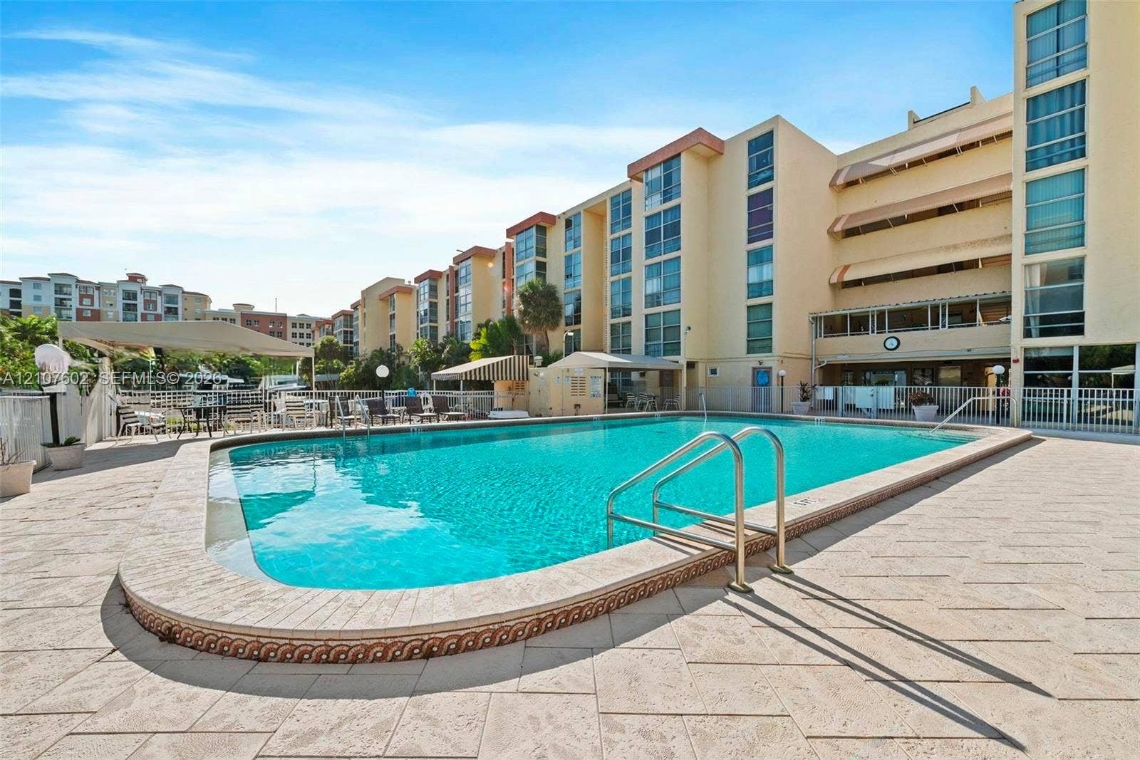 210 172nd Street, #542, Sunny Isles Beach, FL 33160 Swimming pool featuring stone-paver decking, metal entry handrails, and a dedicated sunshade structure