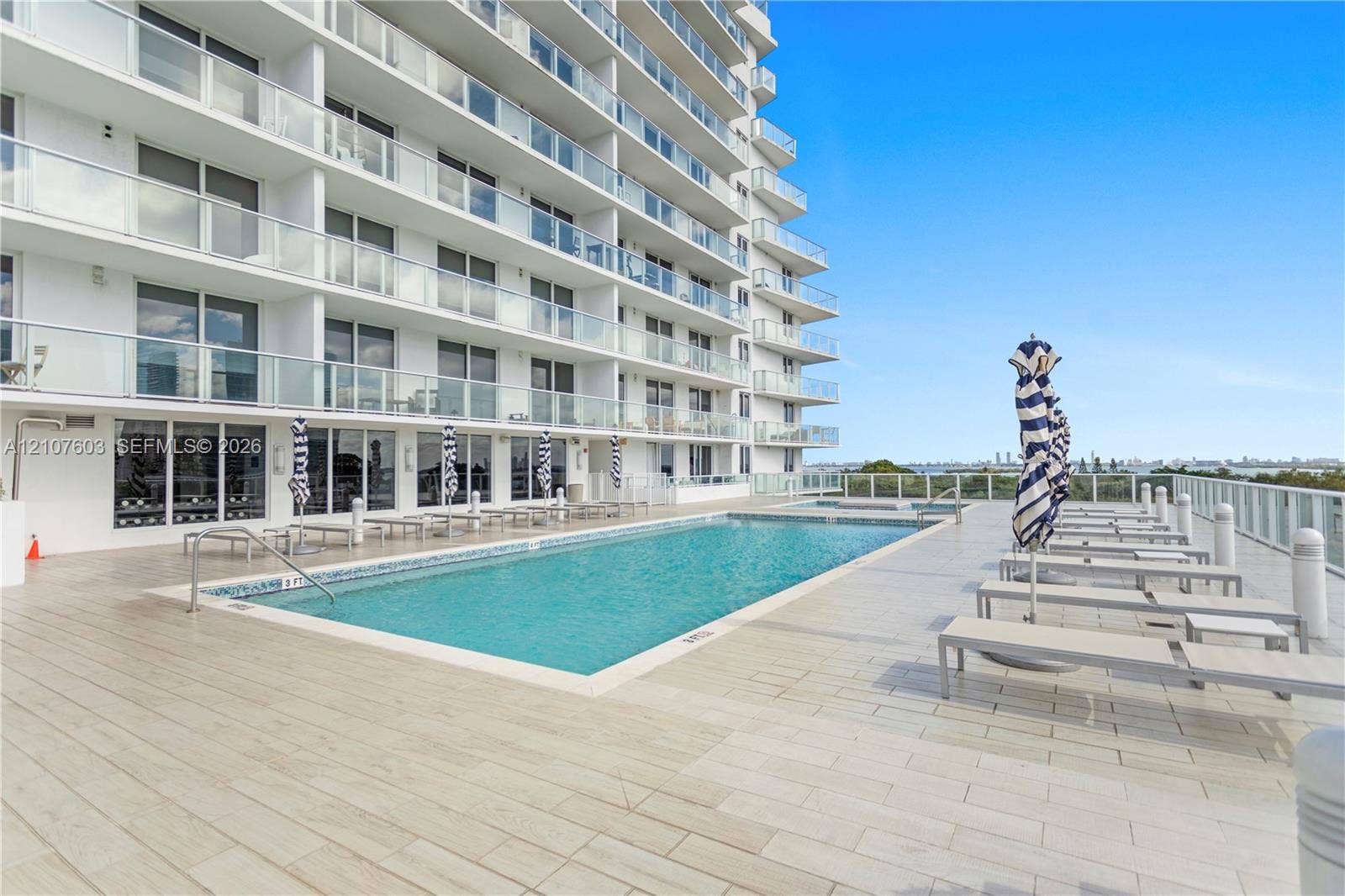 4250 Biscayne Boulevard, #1418, Miami, FL 33137 In-ground swimming pool with tile border, sprawling ceramic tile pool deck, and multi-story high-rise building featuring private glass-paneled balconies