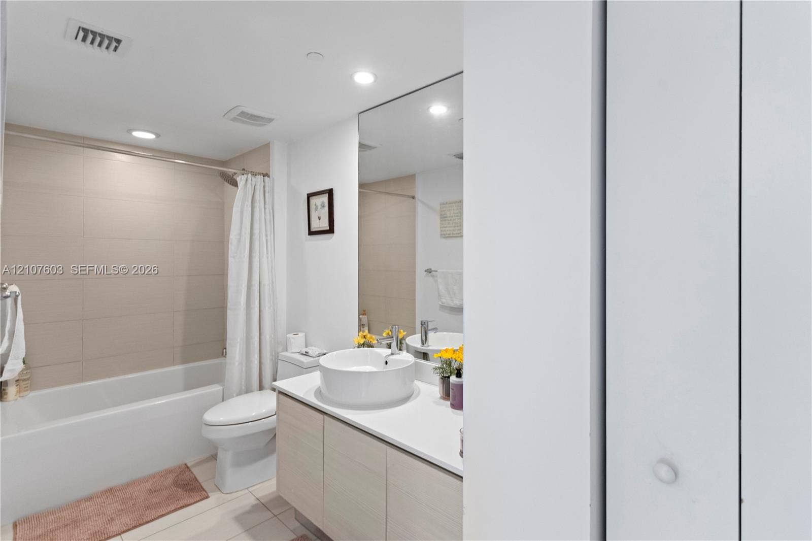 4250 Biscayne Boulevard, #1418, Miami, FL 33137 Bathroom featuring a vanity with wood-finish cabinetry, a white countertop, a circular vessel sink, wall-spanning mirror, and a tub-shower combination with large-format wall tile