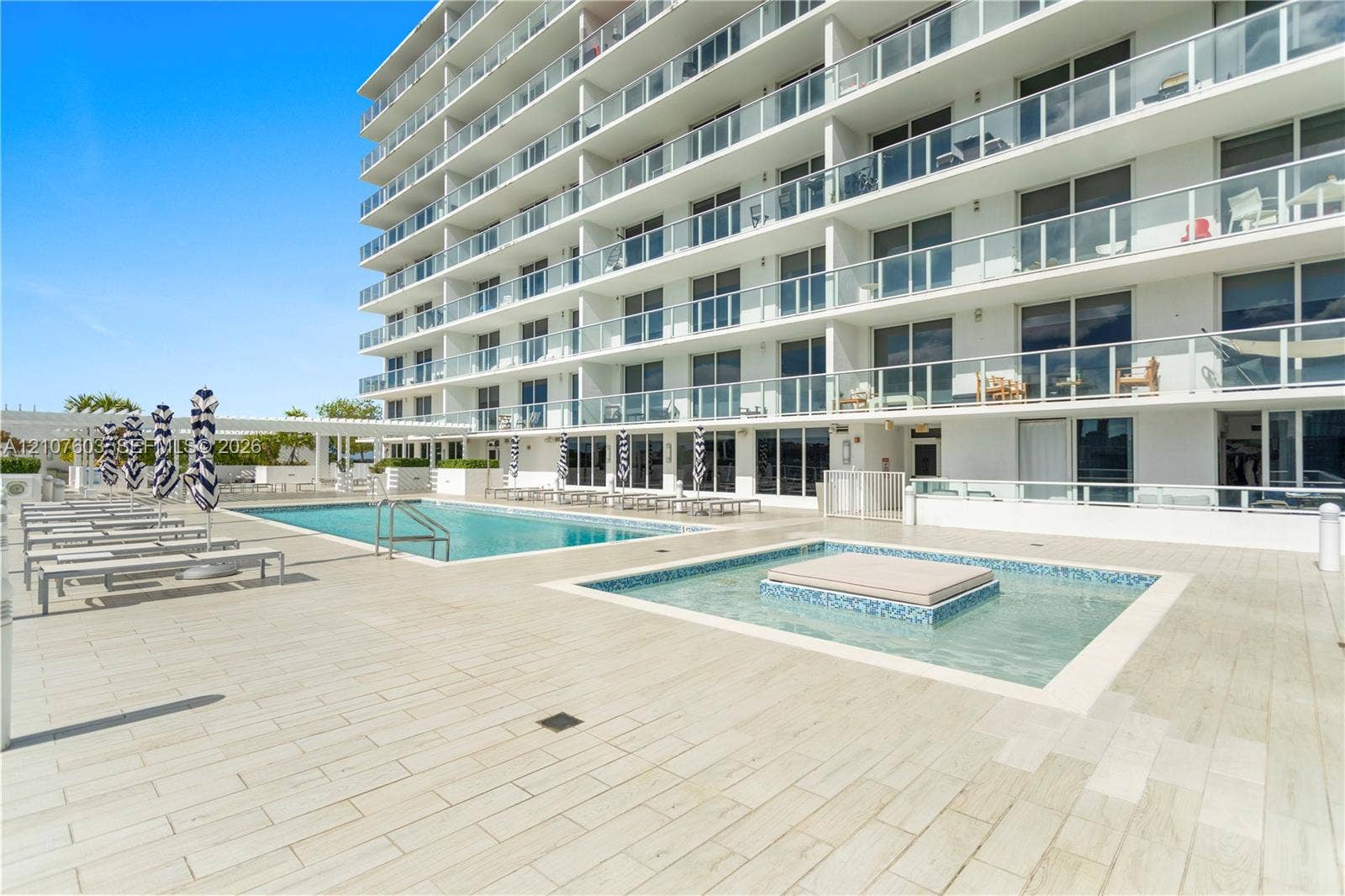 4250 Biscayne Boulevard, #1418, Miami, FL 33137 Poolside terrace featuring an in-ground swimming pool, tiled spa, wood-finish porcelain decking, and multi-story building exterior with glass-railed balconies