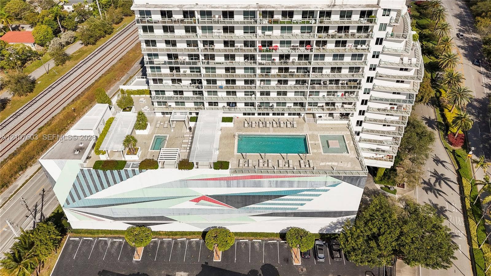 4250 Biscayne Boulevard, #1418, Miami, FL 33137 Multi-story residential building featuring a sprawling elevated terrace with a swimming pool, multiple pergola structures, concrete hardscaping, and decorative mural exterior facade
