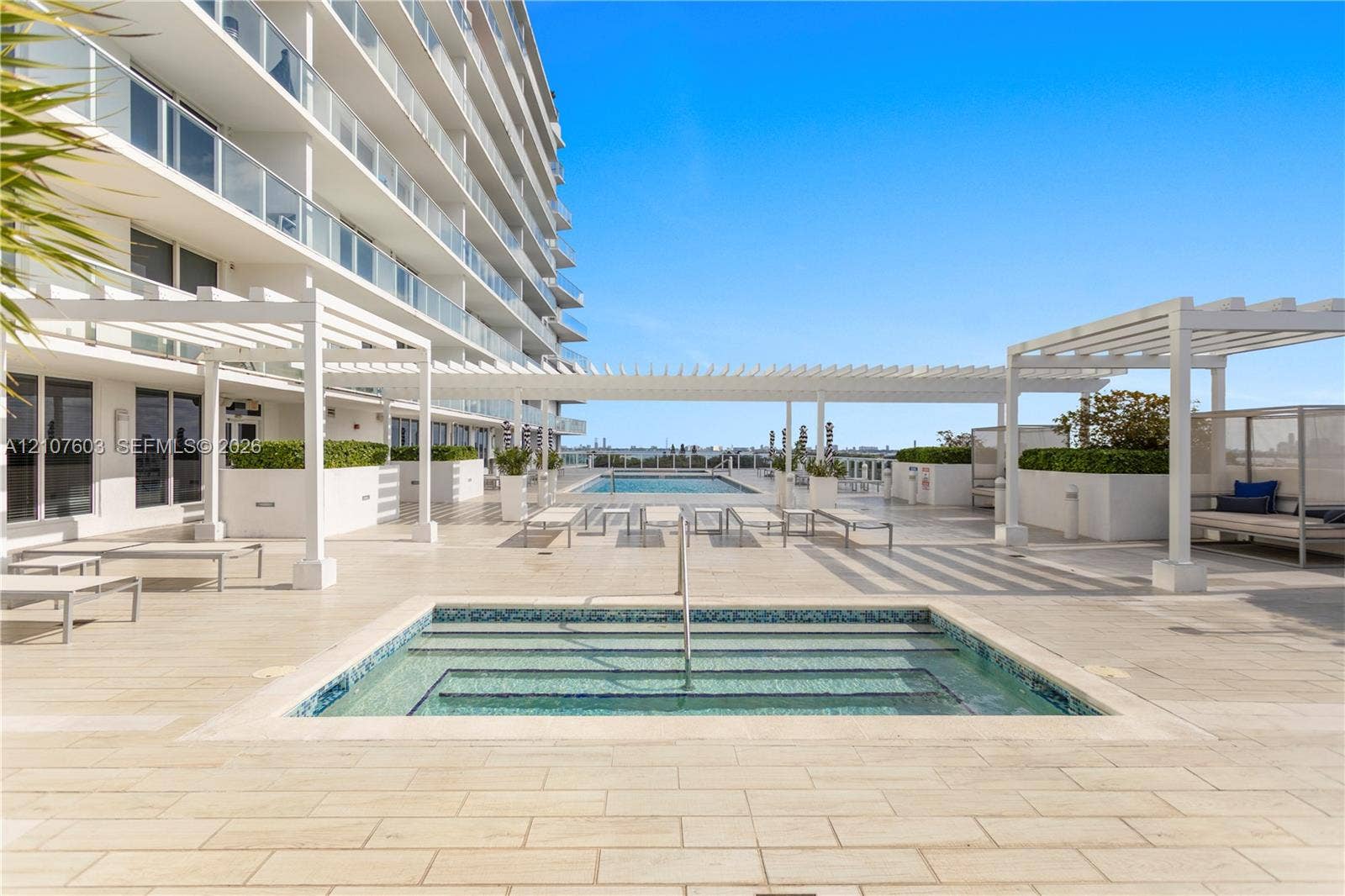 4250 Biscayne Boulevard, #1418, Miami, FL 33137 Outdoor terrace featuring a tiled deck, built-in swimming pool with step entry, mosaic tile accents, white pergola structures, and integrated concrete planters
