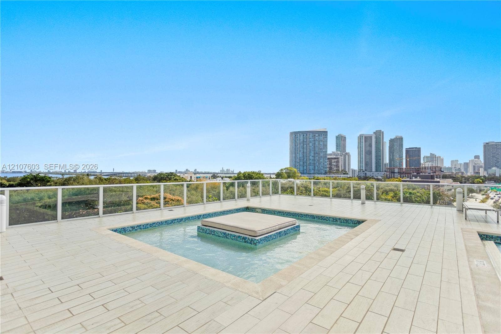 4250 Biscayne Boulevard, #1418, Miami, FL 33137 Rooftop terrace featuring large-format tile flooring, a central built-in water feature with mosaic tile accents, a glass panel railing system, and an expansive cityscape backdrop