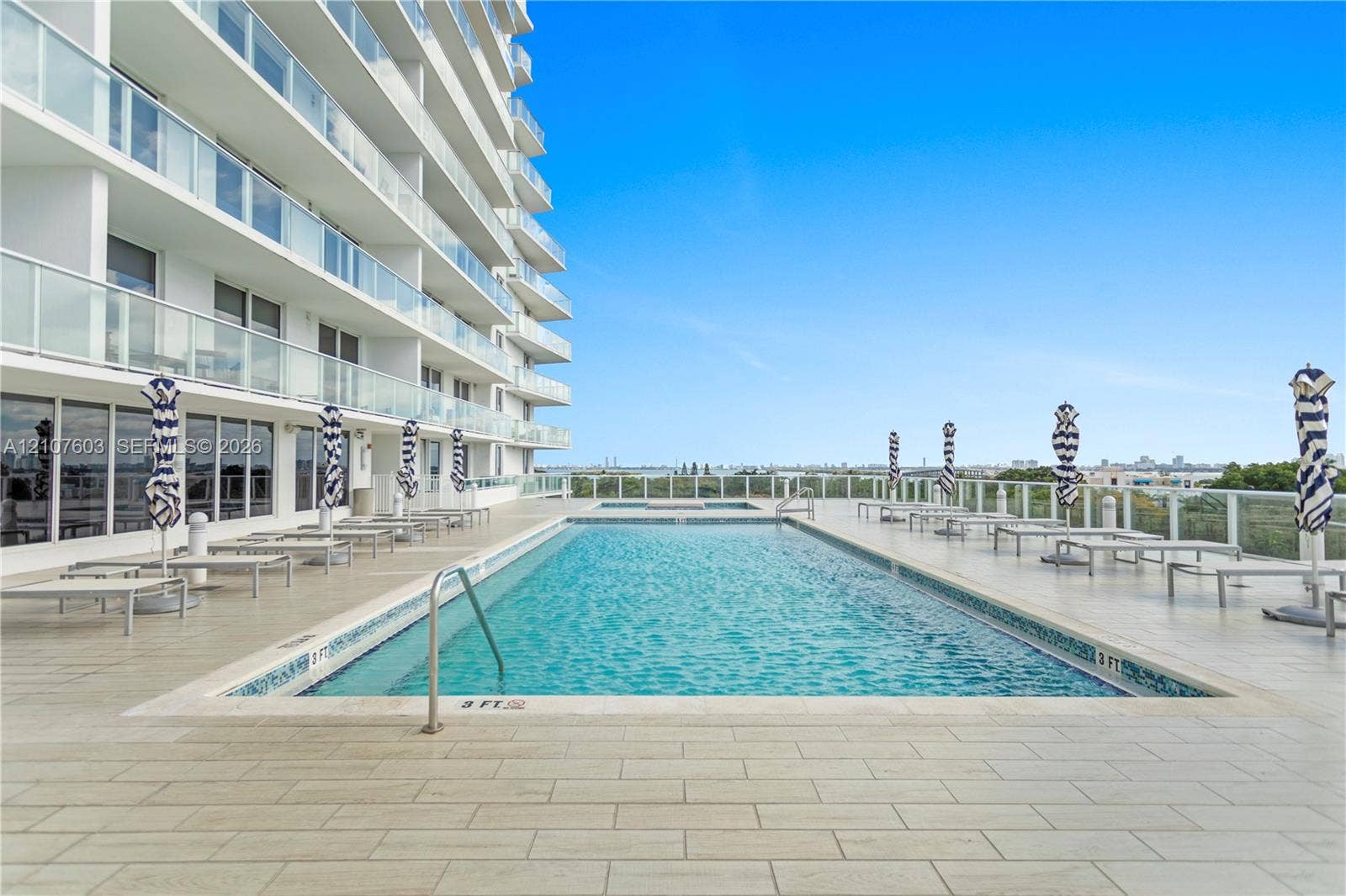 4250 Biscayne Boulevard, #1418, Miami, FL 33137 Rectangular swimming pool featuring a tile surround, metal handrail, perimeter glass panel fencing, and wood-finish tile decking