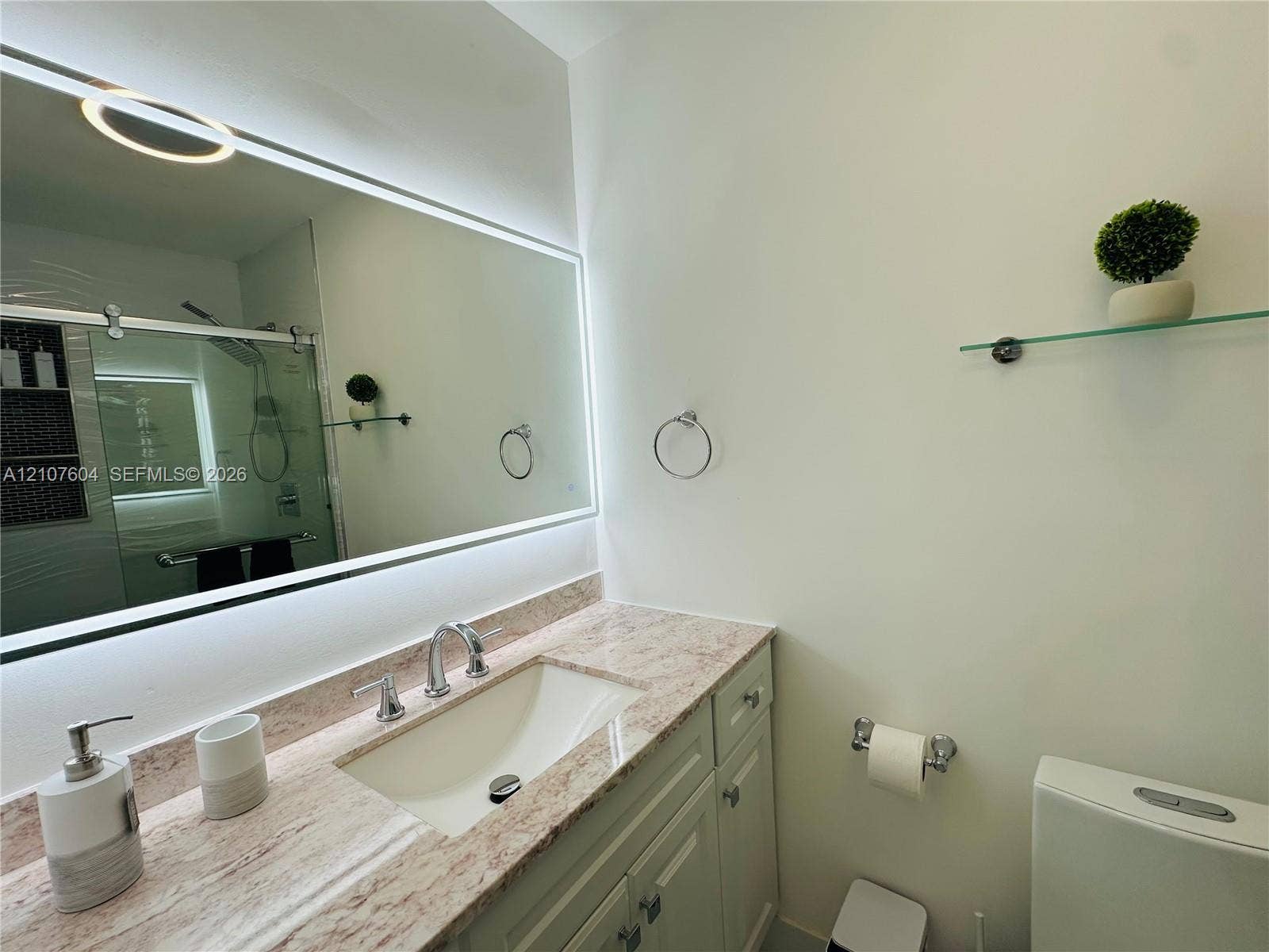 120 S 56th Avenue, Hollywood, Hollywood, FL 33023 Bathroom vanity featuring a stone countertop with an undermount sink, widespread metal faucet, wall-mounted backlit mirror, and glass shelf