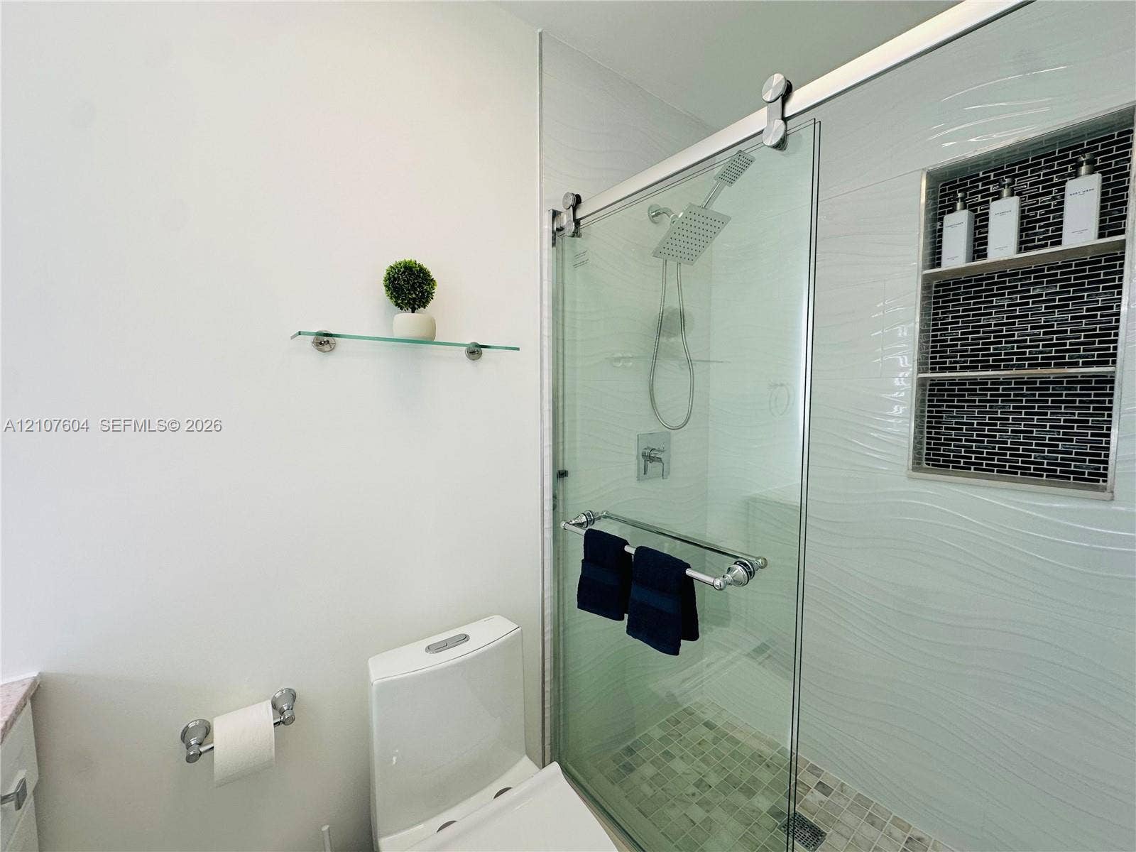 120 S 56th Avenue, Hollywood, Hollywood, FL 33023 Walk-in shower featuring a sliding glass door, rainfall showerhead, textured tile surround, mosaic stone-finish floor, and a built-in recessed tiled niche