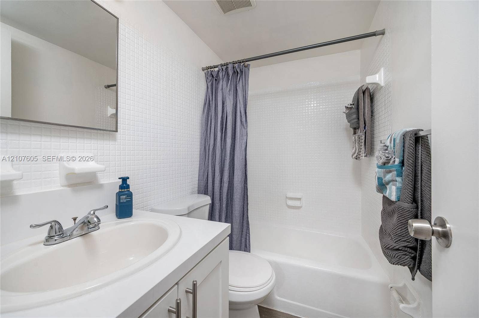 444 SW 27th Avenue, #42, Miami, Miami, FL 33135 Bathroom featuring a white vanity with a composite countertop and integrated sink, a frameless wall-mounted mirror, white square-tiled wall surround, and a white tub-shower combination