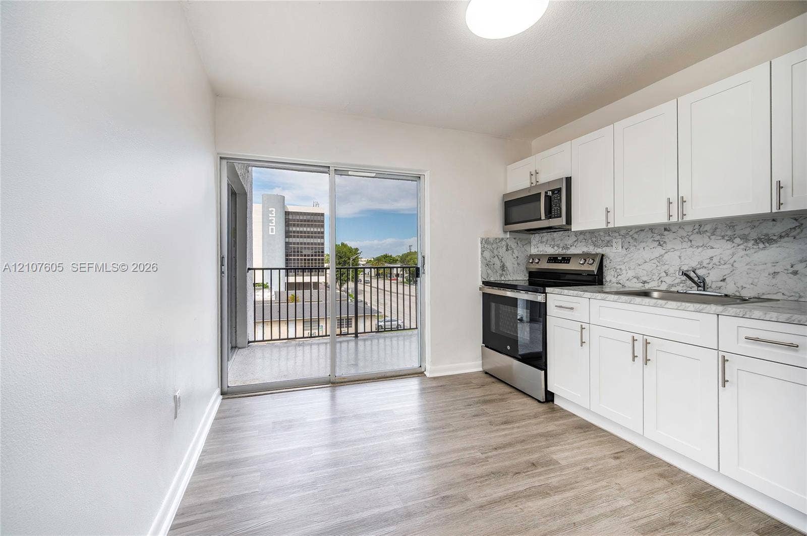 444 SW 27th Avenue, #42, Miami, Miami, FL 33135 Kitchen featuring white shaker-style cabinetry, stone-patterned backsplash, stainless steel appliances, wood-finish flooring, and a sliding glass door opening to a private balcony